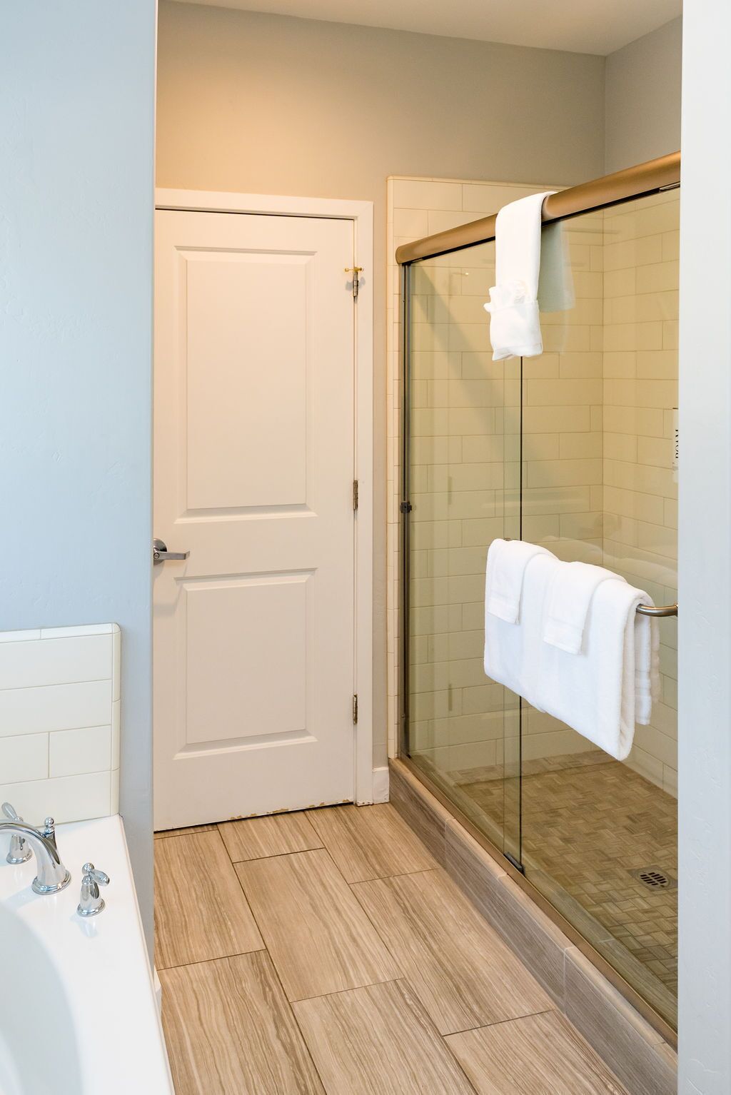 A bathroom with a white door, a glass shower enclosure, and a white bathtub.