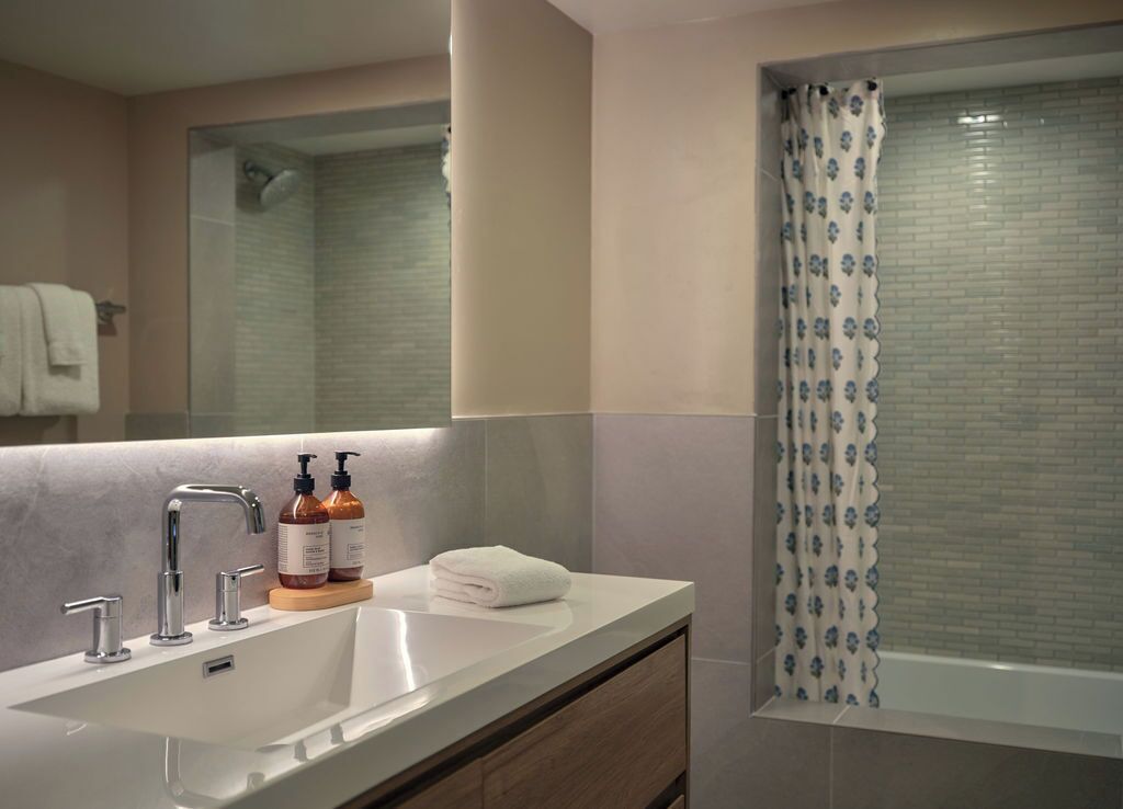 A modern bathroom with a large sink, a mirror, and a shower with a patterned curtain.