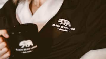 Una persona sosteniendo una taza negra con un logo de oso y la inscripción 'BLACK BEAR LODGE'.