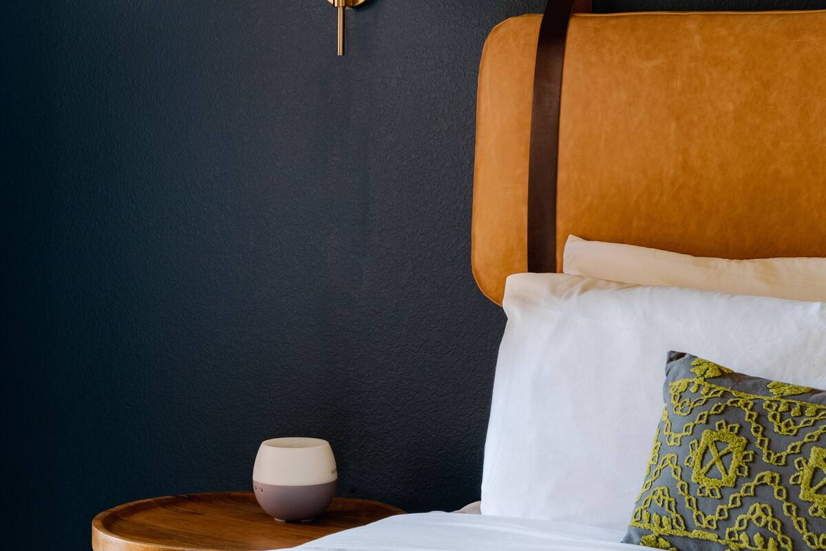 Een slaapkamer met een bed, nachtkastje, lamp en een wandplank.