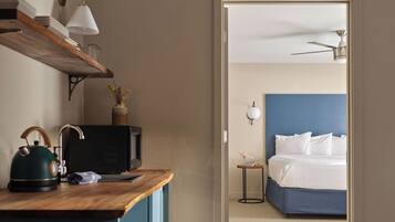 Une chambre d’hôtel avec un bureau en bois, un lit avec une tête de lit bleue, un ventilateur de plafond et une table de chevet avec une lampe.