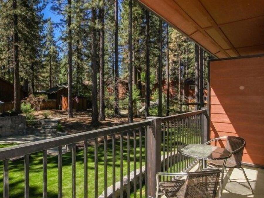 A balcony with a view of a forest, a table with chairs, and a wooden building.