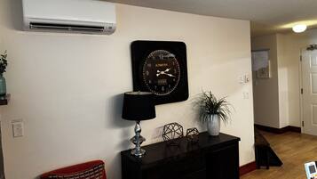 Una sala de estar con un reloj negro, una lámpara, una planta en maceta y una chimenea en una esquina.