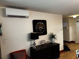 A living room with a black clock, a lamp, a potted plant, and a fireplace in the corner.