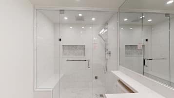 A modern bathroom with a glass shower enclosure, a marble-tiled floor, and a large mirror.