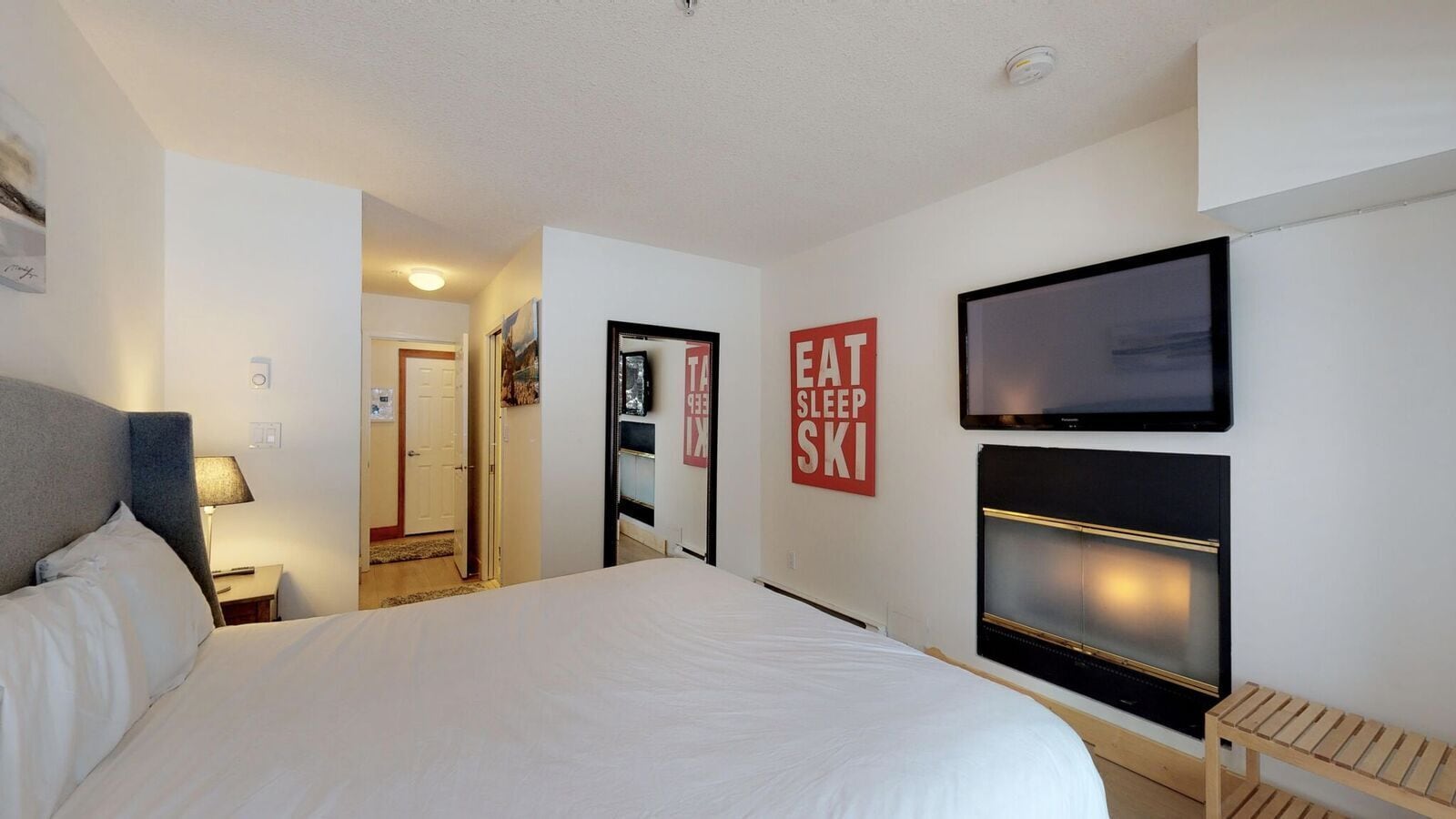Una habitación de hotel con una cama grande, un televisor montado en la pared y un letrero que dice 'EAT SLEEP SKI'.