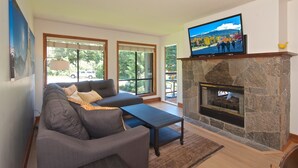 Una sala de estar con chimenea de piedra, un televisor de pantalla plana montado arriba, un sofá gris y una mesa de centro.