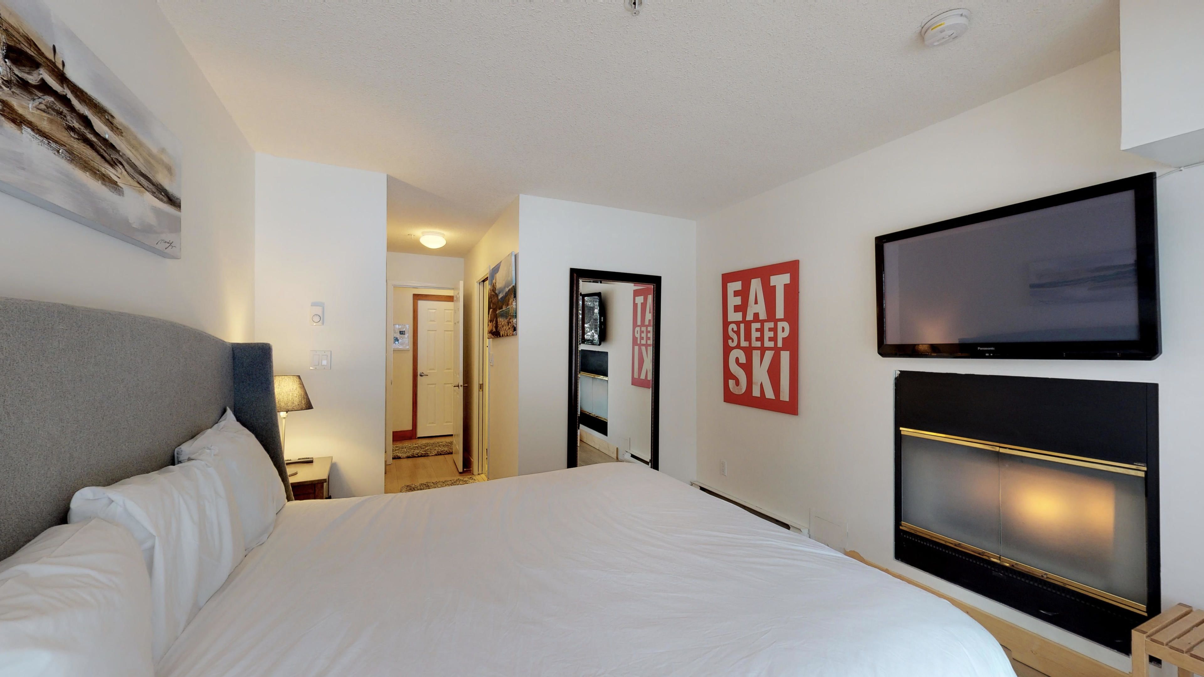 A hotel room with a large bed, a flat-screen TV, and a mirror.