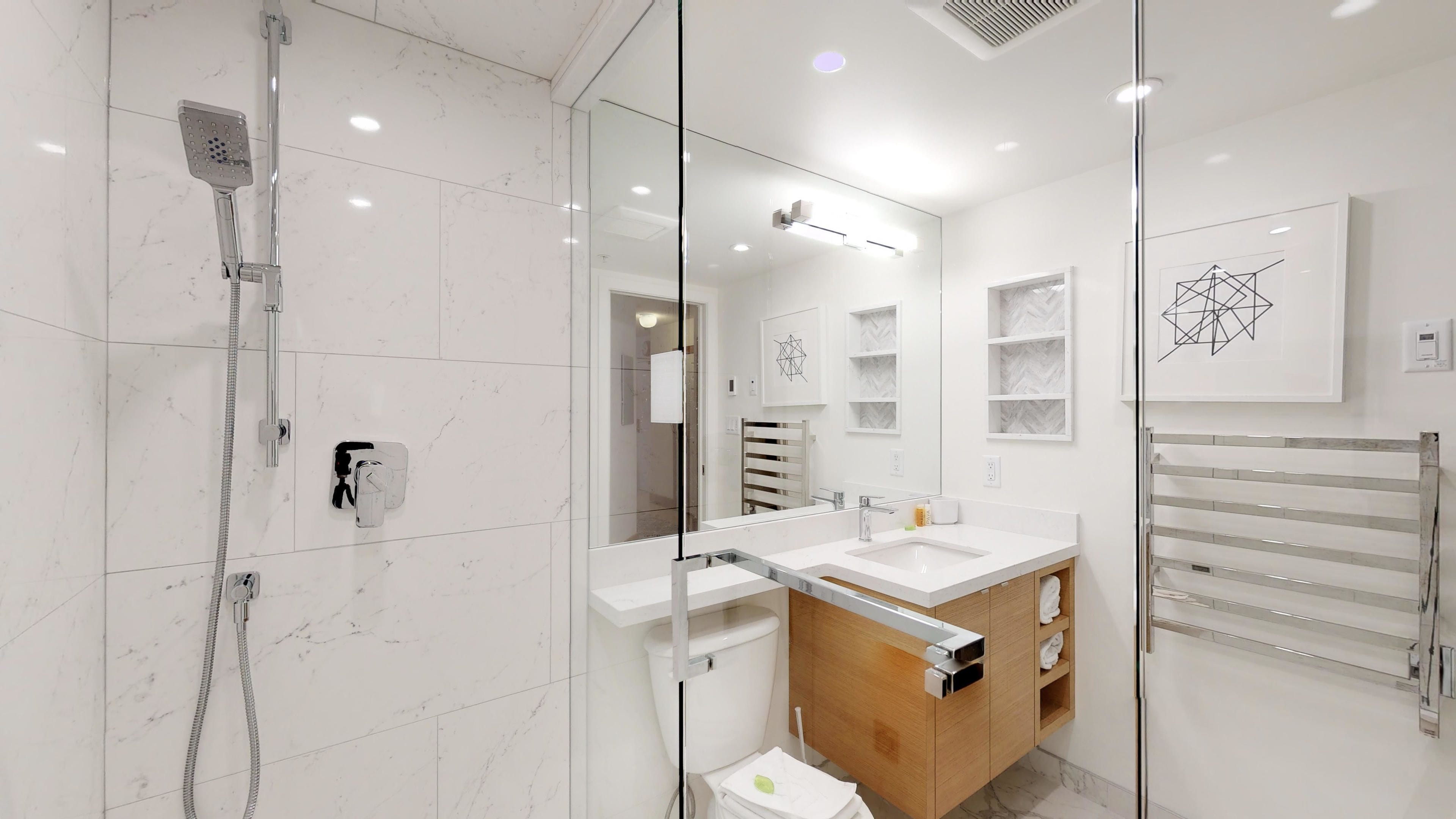 Un baño moderno con ducha envuelta en vidrio, tocador de madera y un espejo grande.