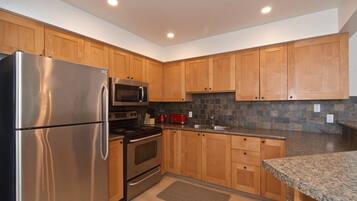 A modern kitchen with wooden cabinets, stainless steel appliances, a granite countertop, and a stone backsplash.