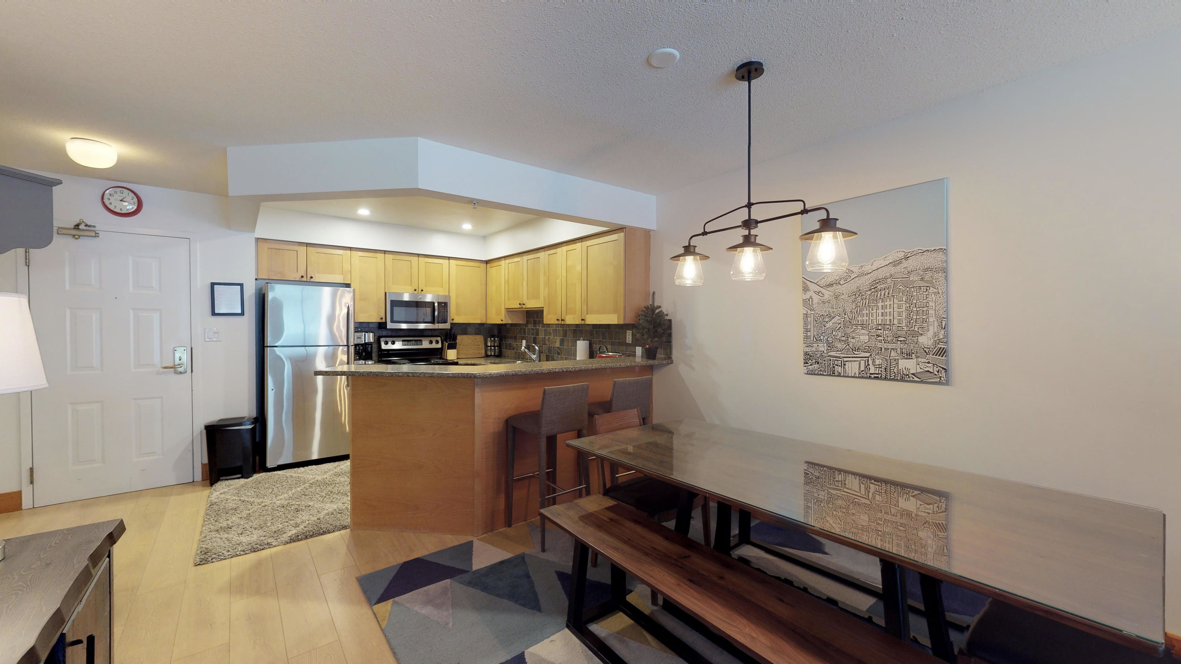 A modern kitchen with a refrigerator, microwave, and stove. There is a dining area with a bench and table.