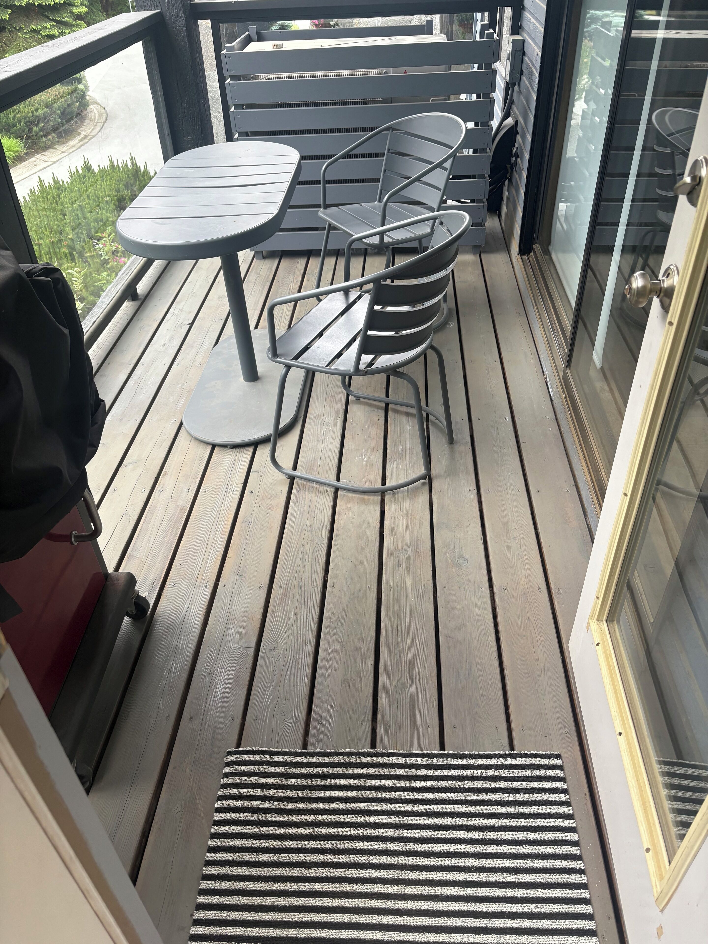 A wooden deck with a table and chairs, a grill, and a glass door.