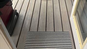 A wooden deck with a table and chairs, a grill, and a glass door.