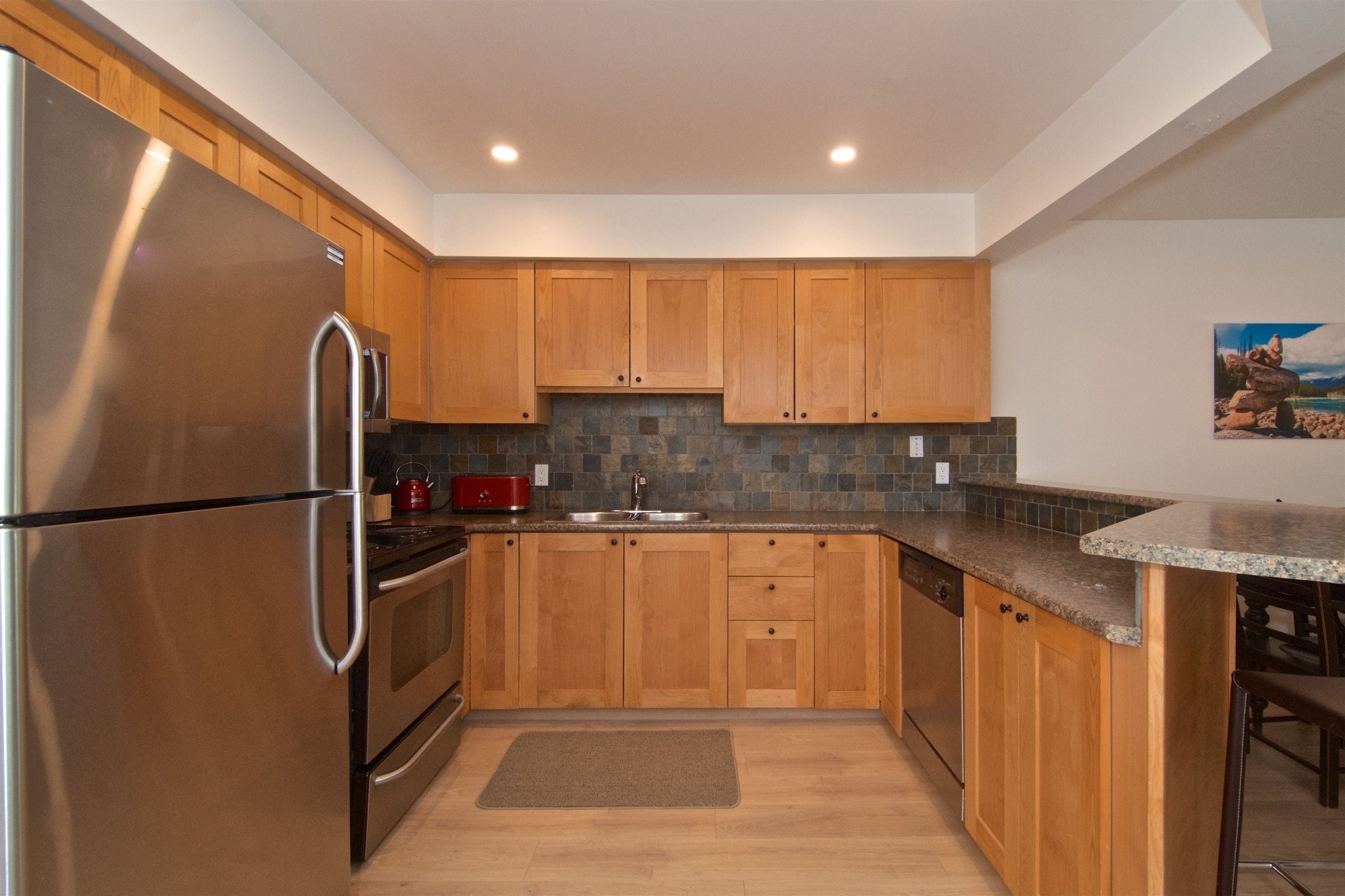 A modern kitchen with wooden cabinets, a stainless steel refrigerator, and a granite countertop.