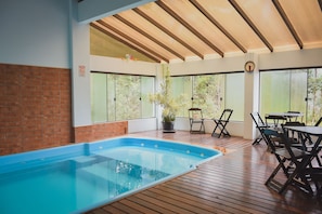 Zona de piscina con plataforma de madera, pared de ladrillo y planta en maceta.