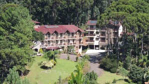 Un hotel de varios pisos con techo de tejas rojas, rodeado de un bosque frondoso.