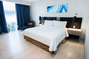 Habitación de hotel moderna con una cama grande, un escritorio y una silla. Se ve la ciudad a través de la ventana.