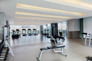 Academia moderna com diversos equipamentos de exercício, amplas janelas e um espaço amplo e arejado.