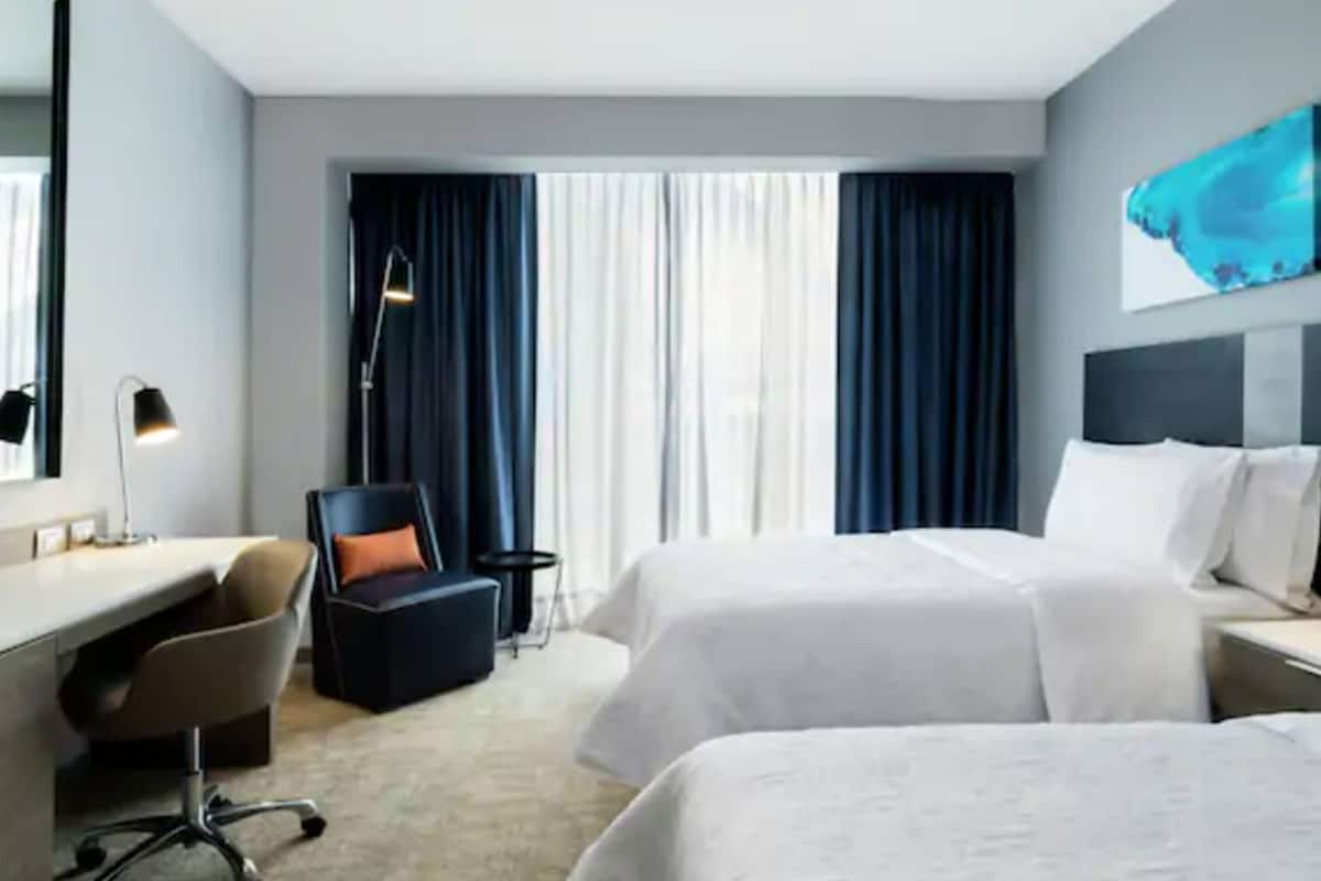 A hotel room with two beds, a desk, a chair, and a large window with curtains.