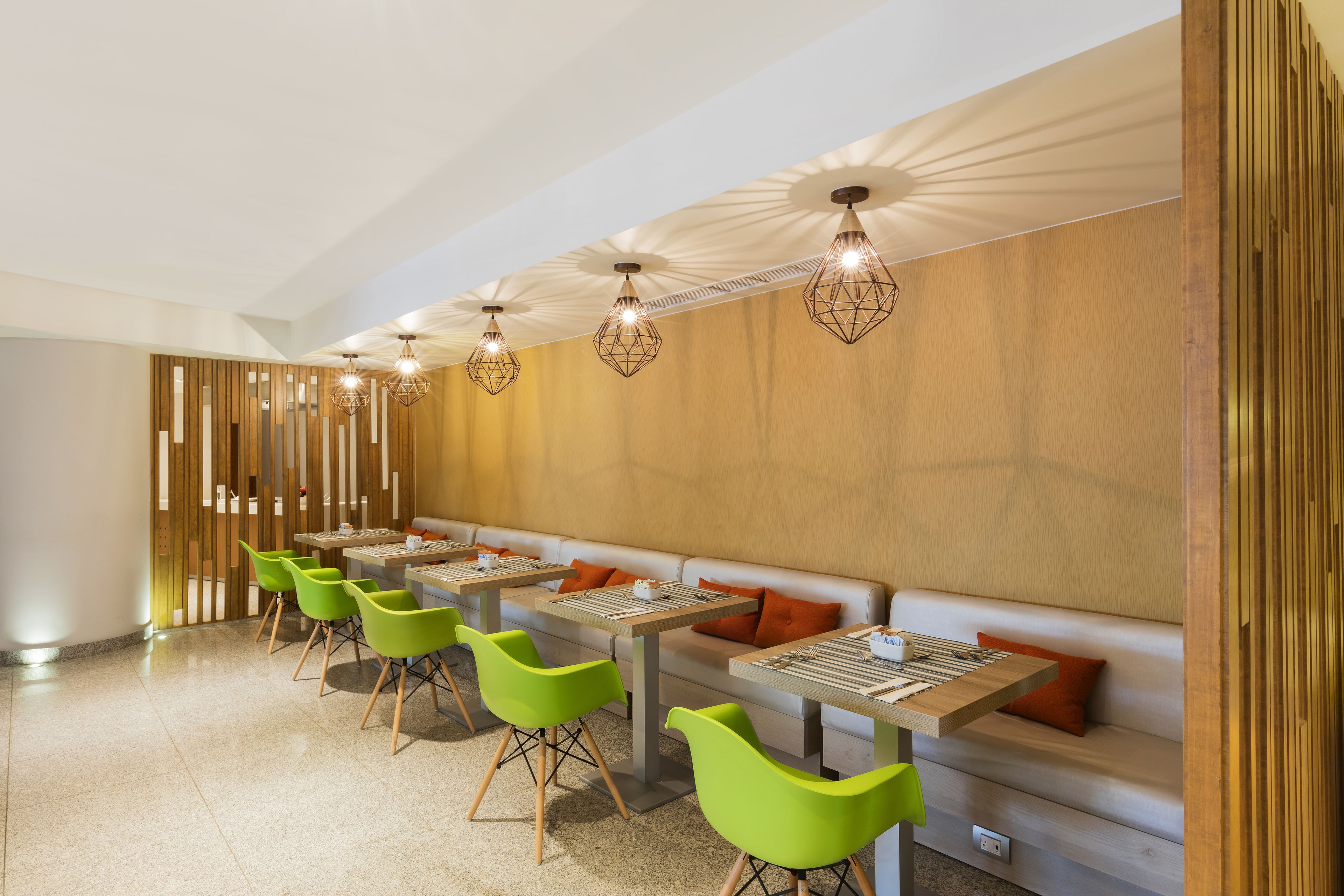 A modern dining area with high tables, green chairs, and a long bench with orange cushions.