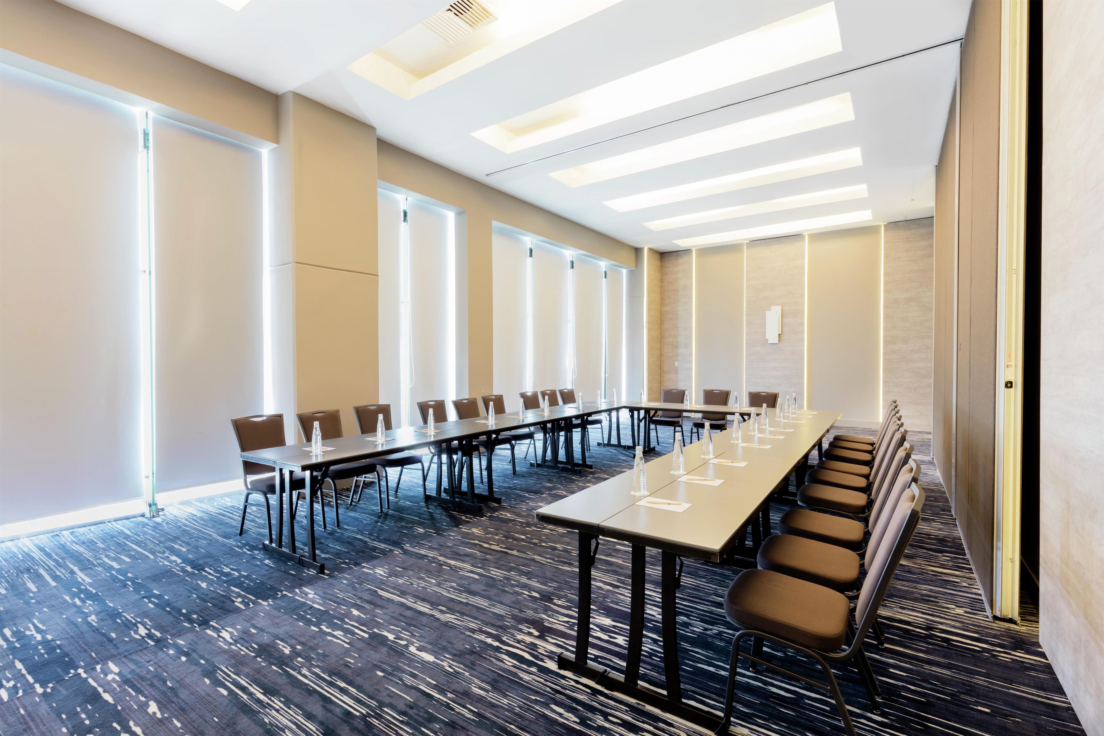 A conference room with long tables, chairs, and a carpeted floor.
