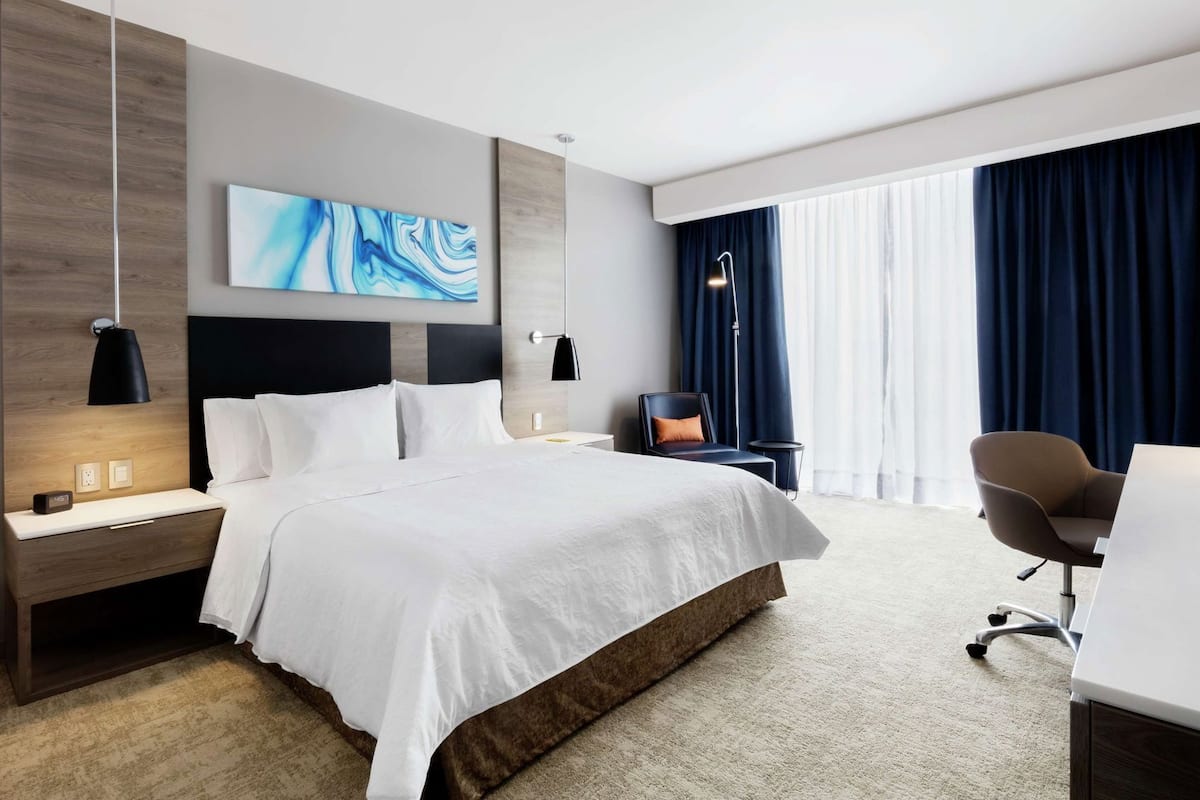 A modern hotel room with a large bed, bedside tables, a desk, and a chair.