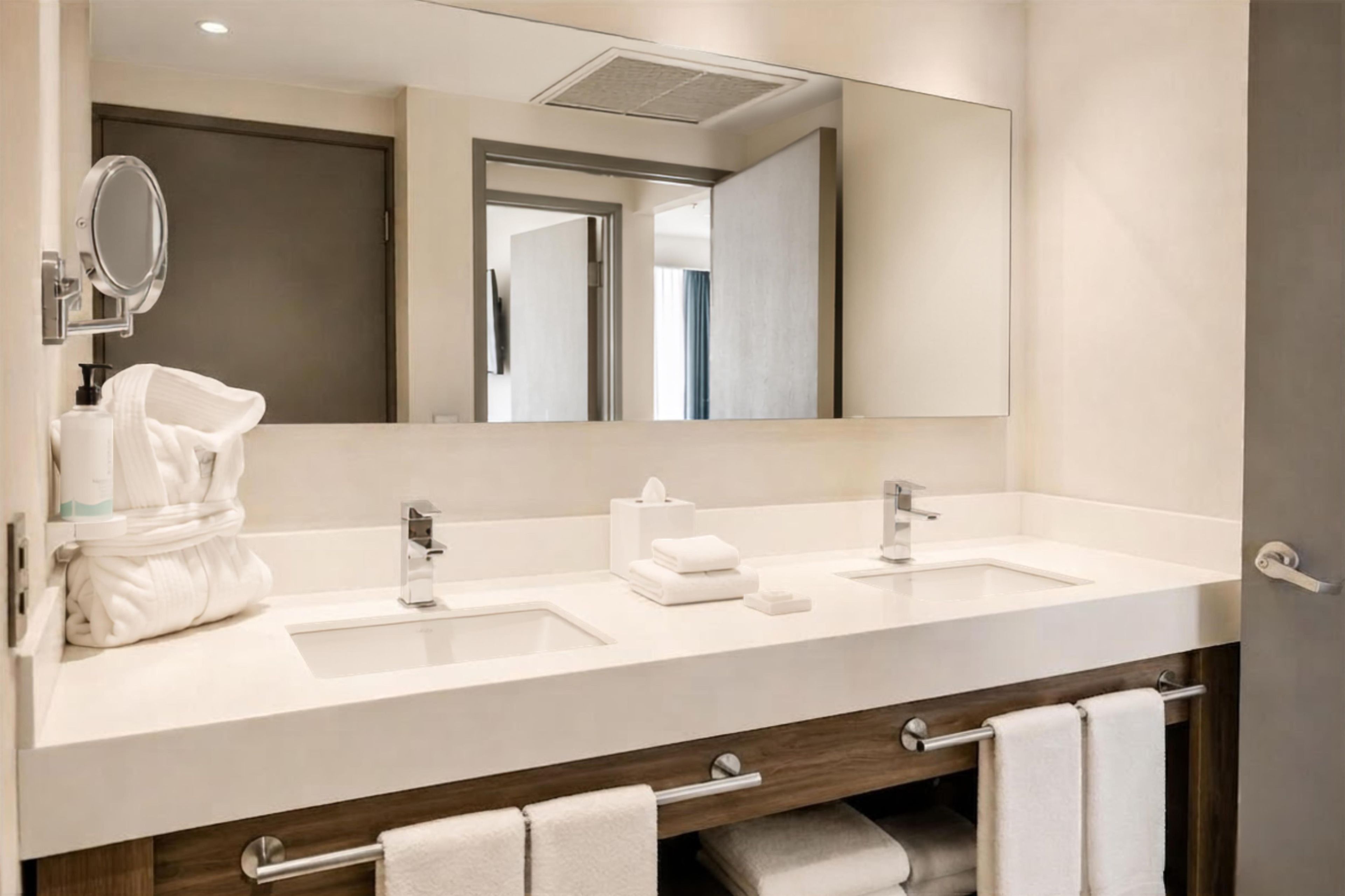 A modern bathroom with two sinks, a large mirror, and a towel rack.