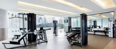 A modern gym with exercise equipment, large windows, and a city view.