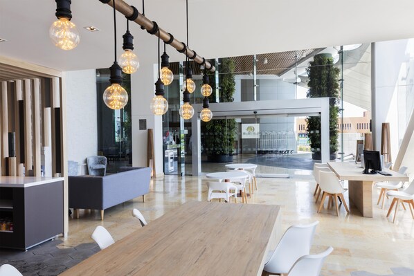 Un espacio de oficina moderno con una larga mesa de madera, sillas blancas y lámparas colgantes.