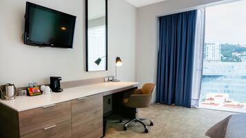 Una habitación de hotel con escritorio, silla, televisor y un ventanal con cortinas.