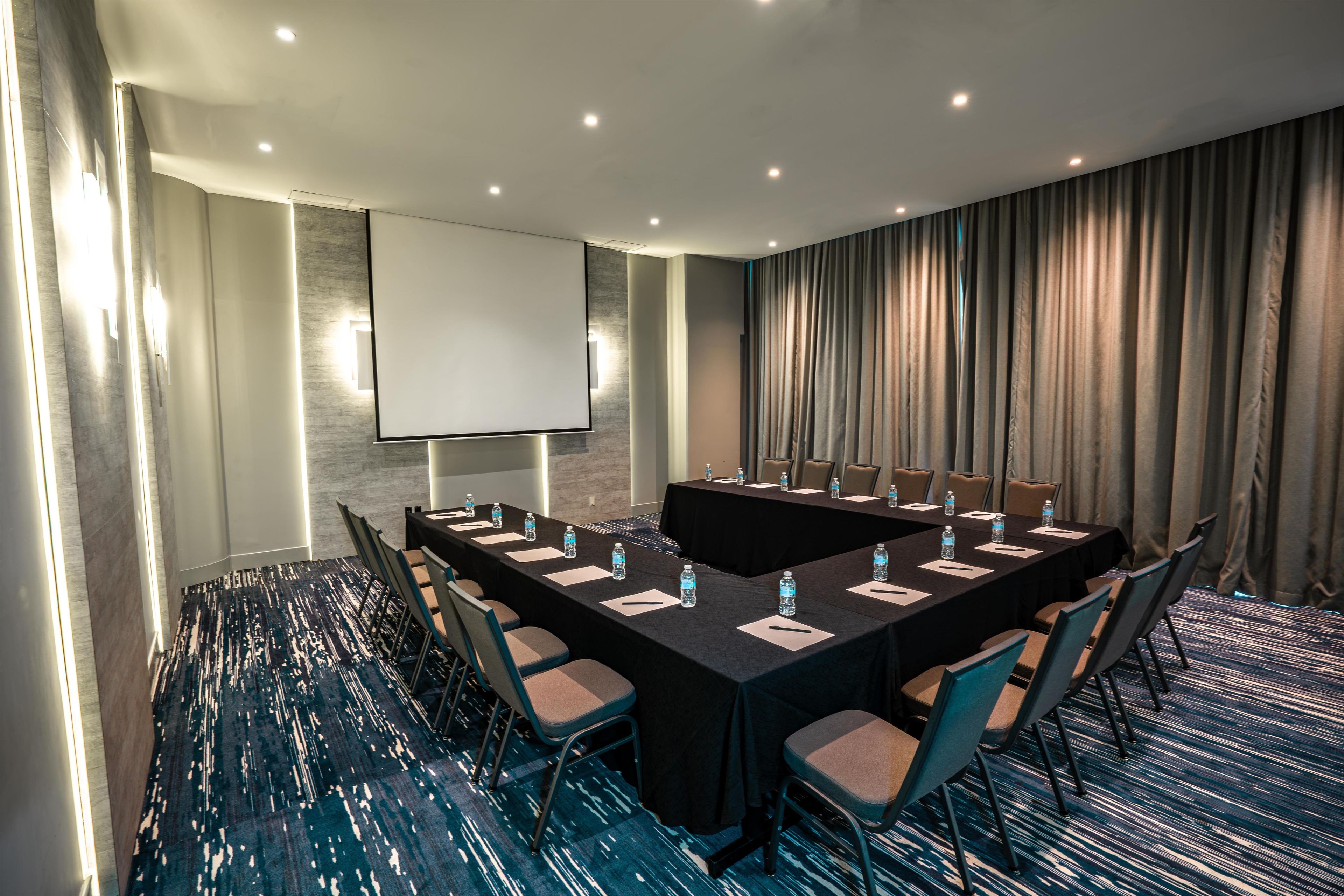 Une salle de conférence équipée d’une longue table, de chaises, d’un écran de projection et d’un distributeur d’eau.
