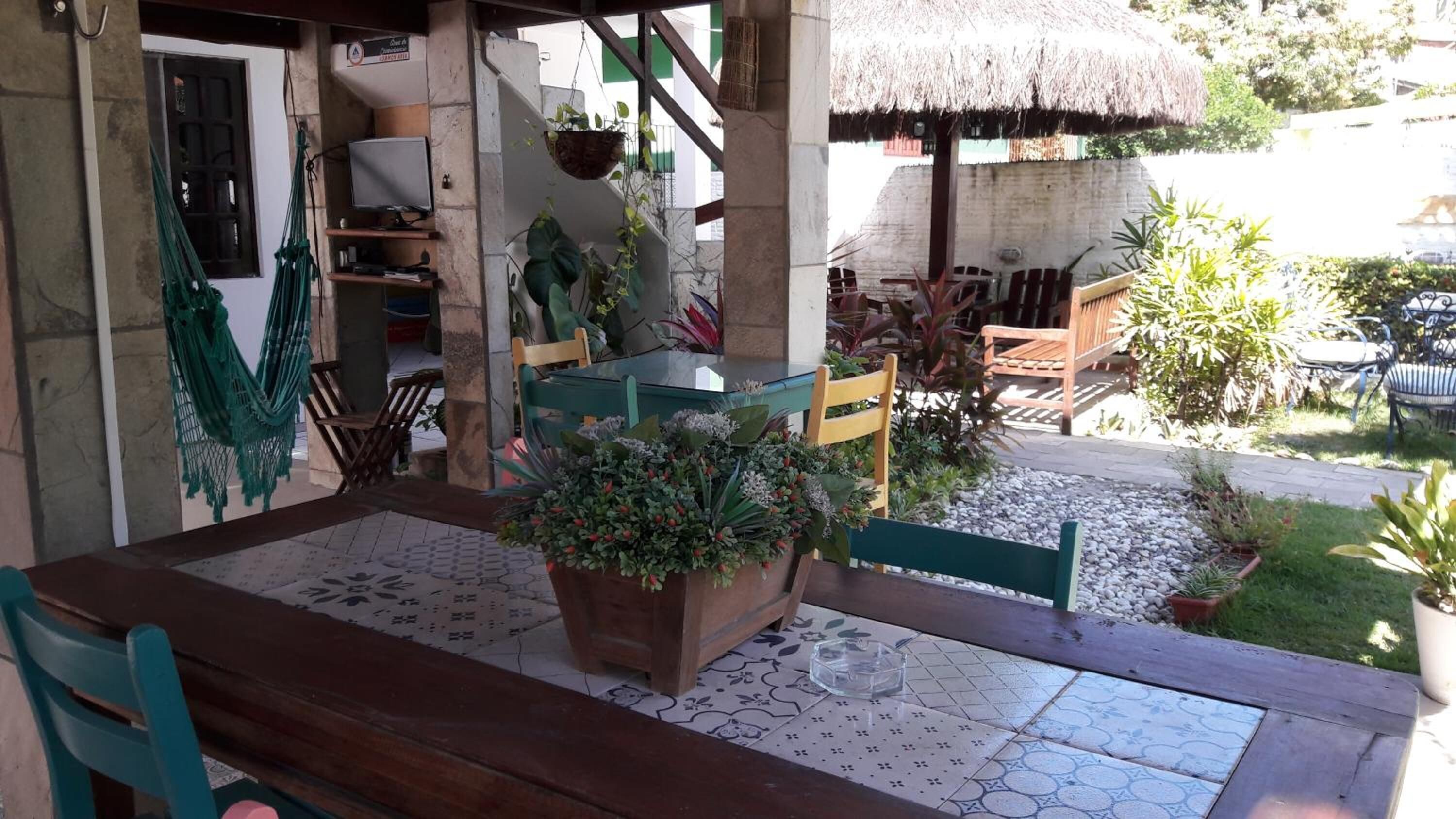 Une terrasse extérieure avec une table et des chaises, entourée de plantes en pot et surmontée d’une structure à toit de chaume.