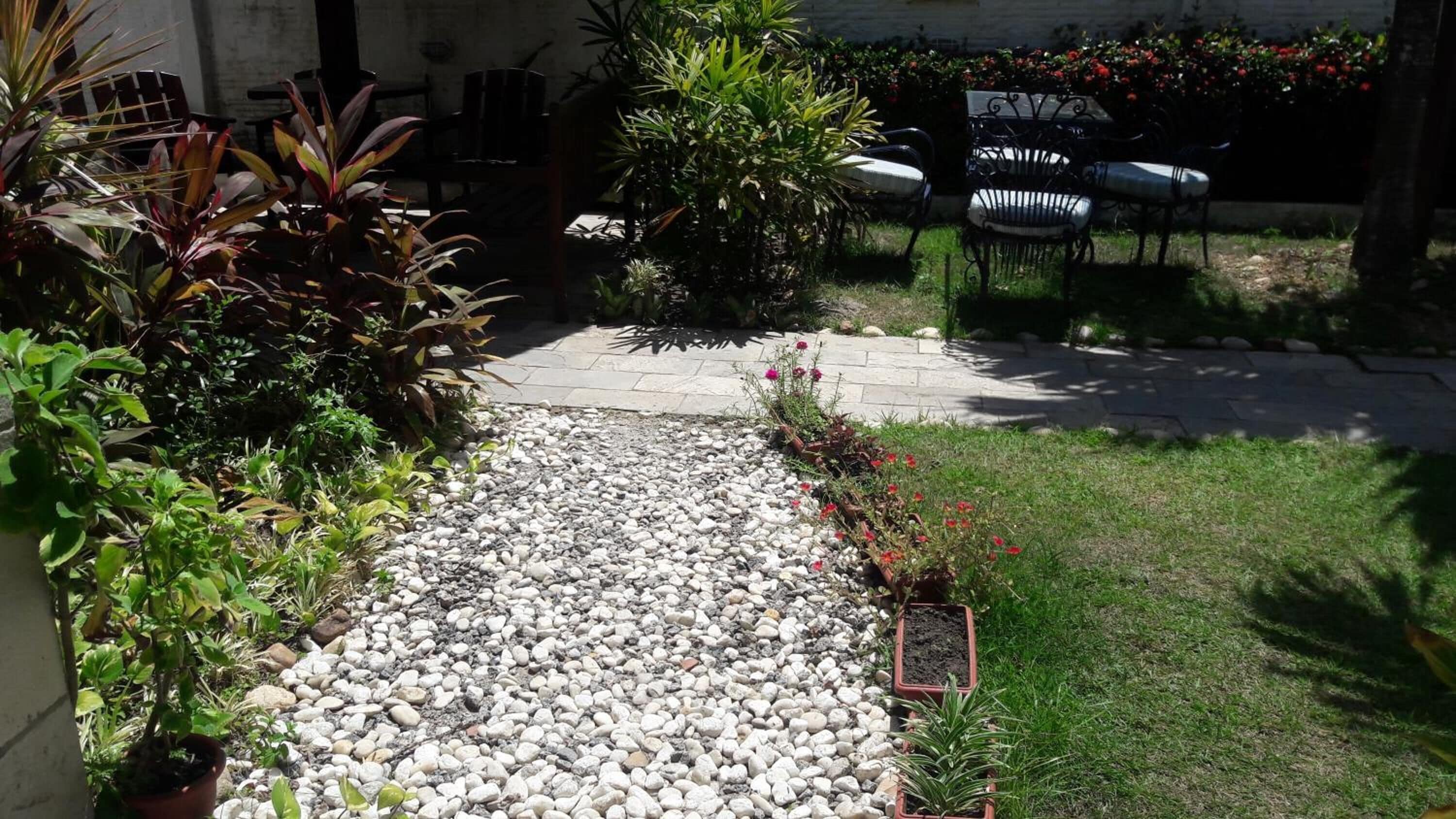 Un jardin avec un chemin de gravier, différentes plantes et du mobilier d’extérieur.