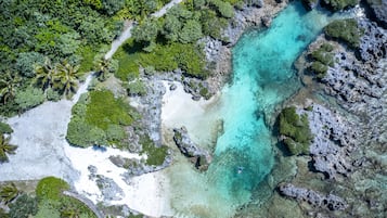 An aerial view of a tropical beach with clear turquoise waters, white sand, and lush greenery.