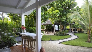 A wooden deck with a table and chairs, surrounded by lush greenery and a thatched-roof structure. - Papaya Villa B&B  (Eton)