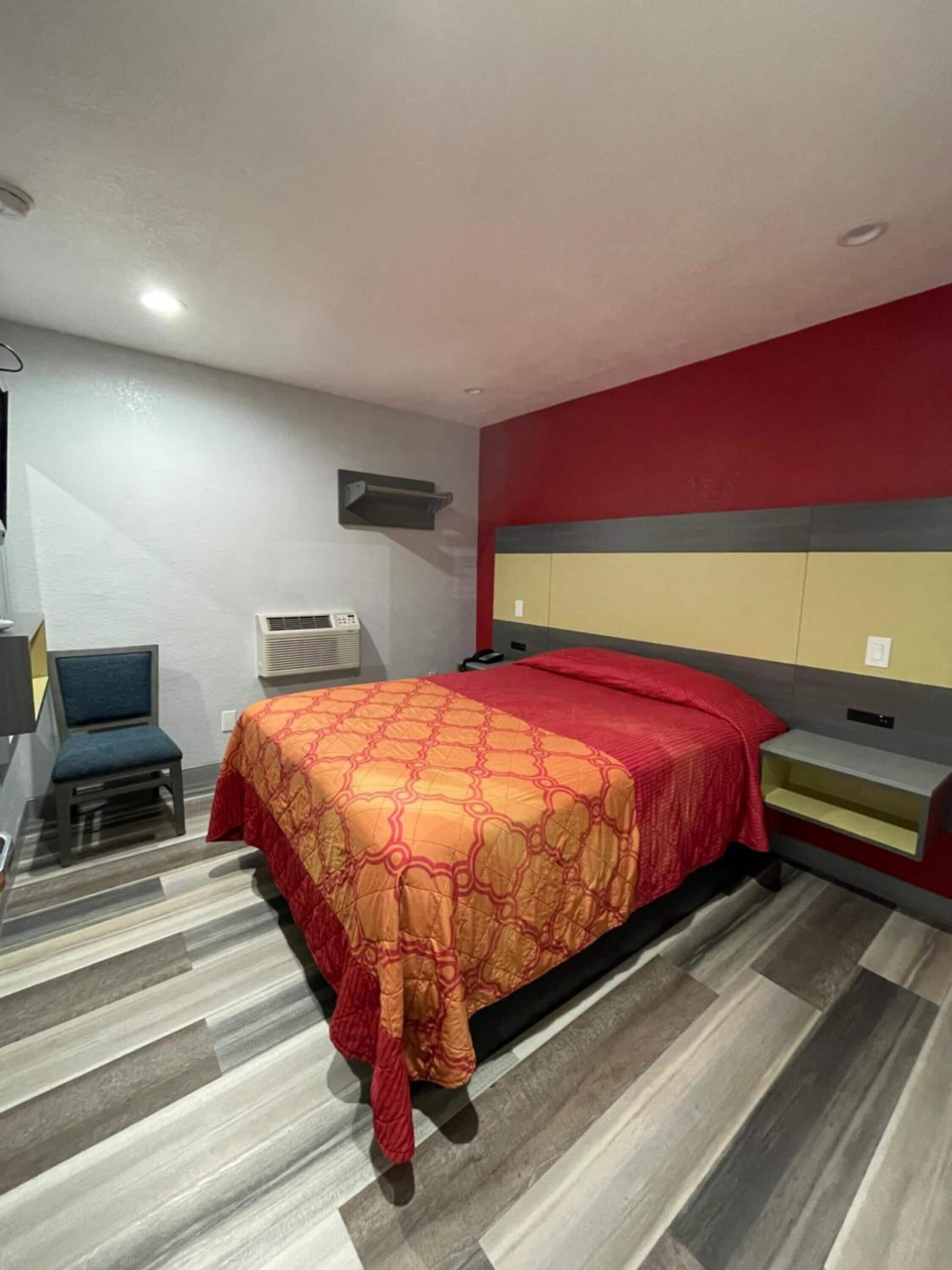 A hotel room with a bed, a chair, a desk, and a wall-mounted air conditioner.