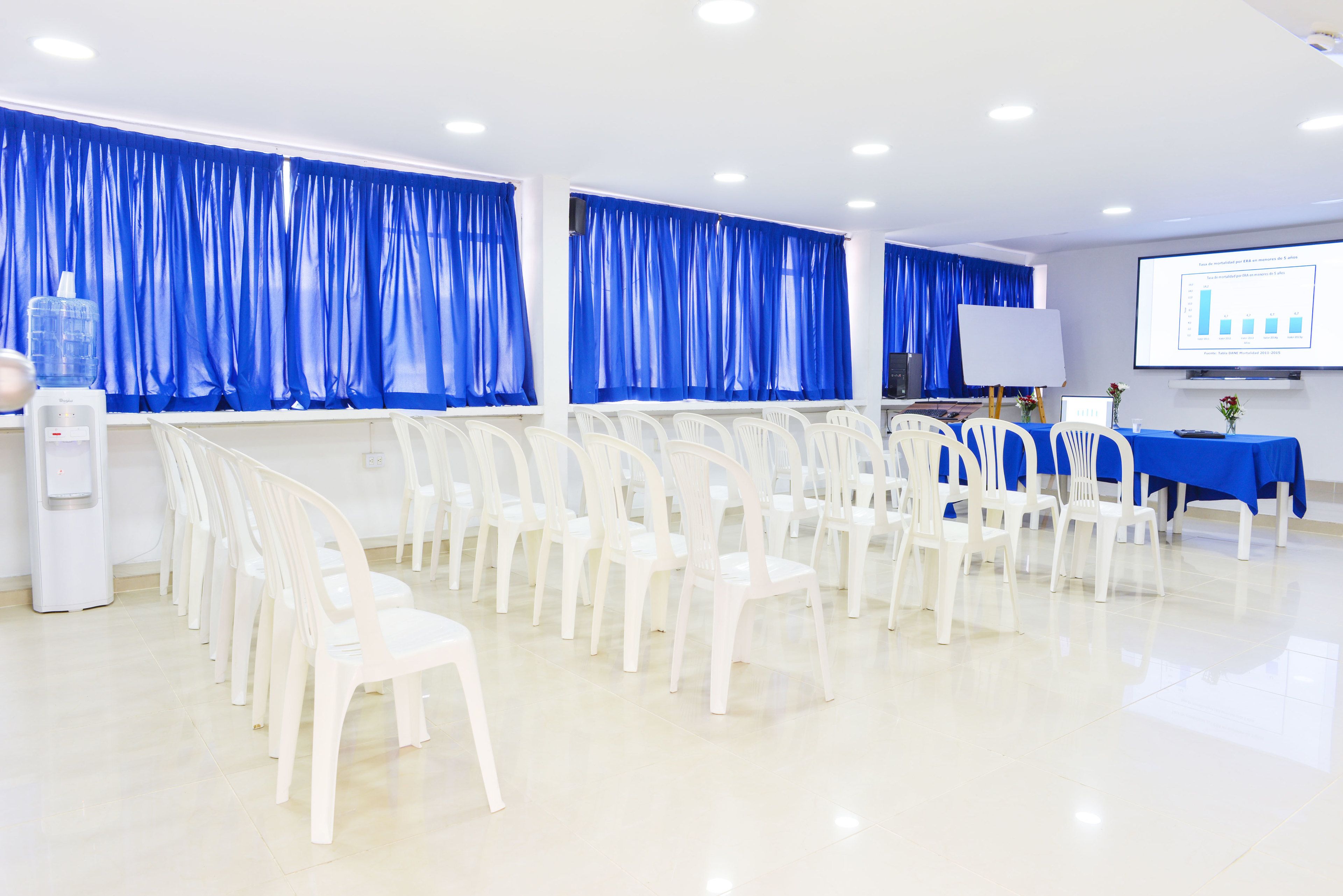 A conference room with rows of white chairs, a projector screen, and a presentation board.