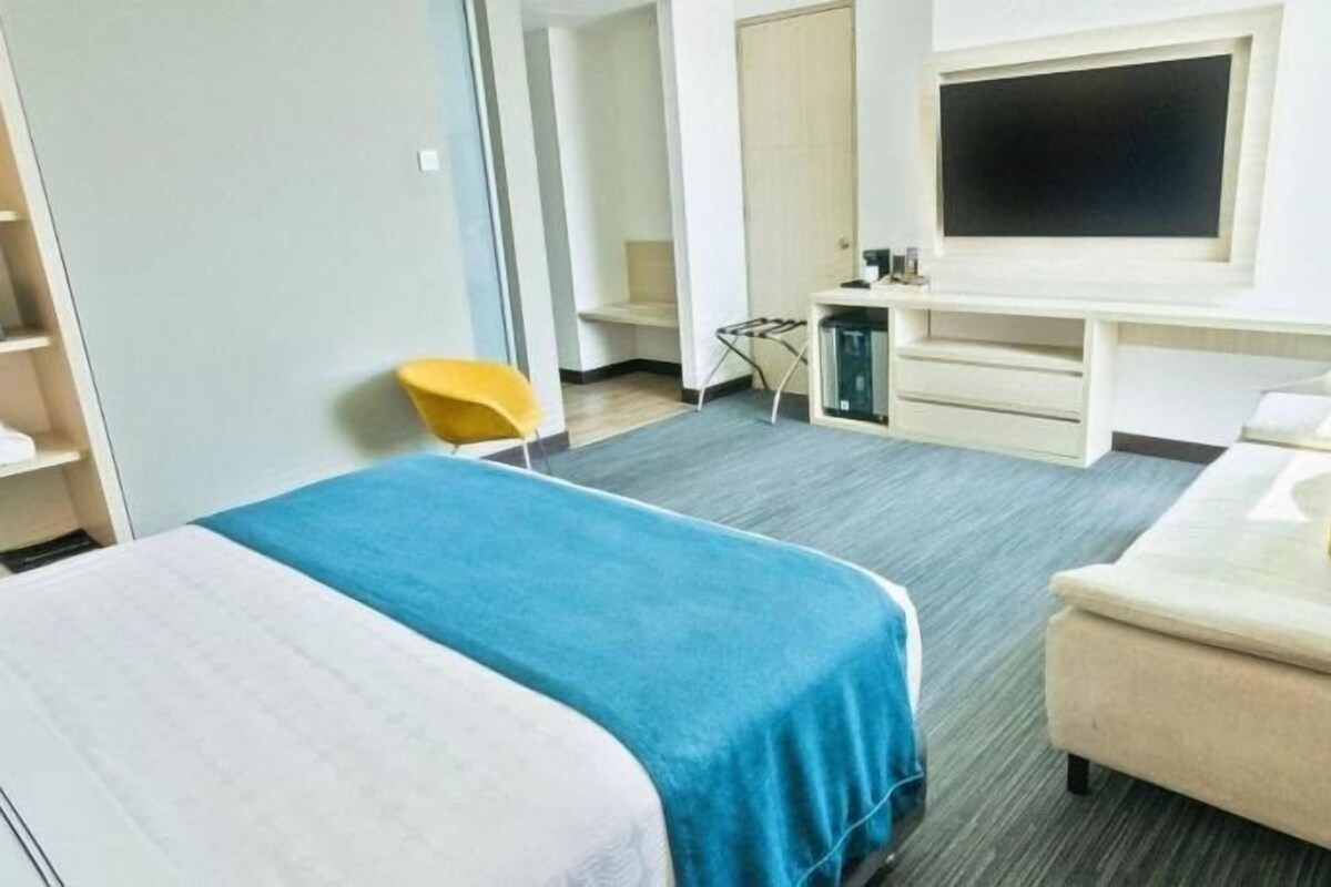 A hotel room with a bed, a sofa, a TV, and a desk.