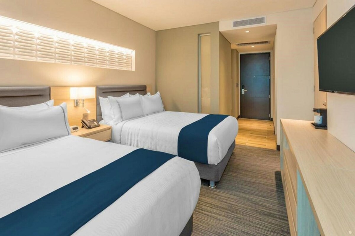 A hotel room with two beds, a desk, a TV, and a bathroom door.