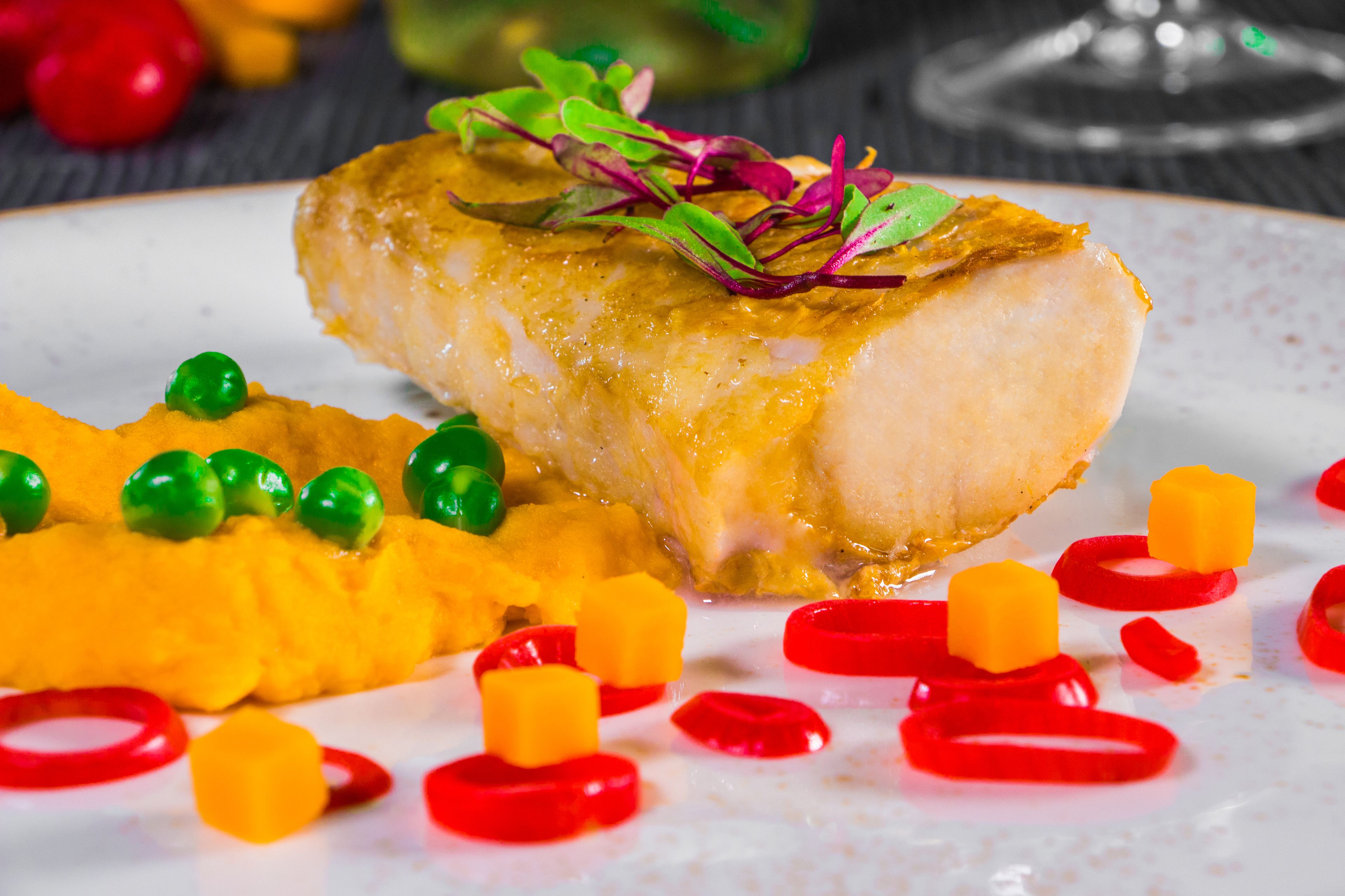 Un plato de comida con un filete de pescado blanco, guisantes verdes y tiras de pimiento rojo.