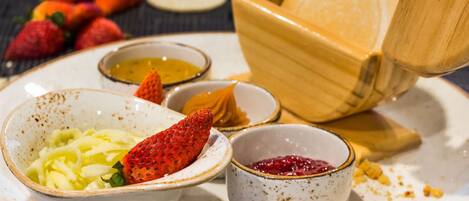 A plate with various food items including sliced apples, strawberries, and small bowls of sauces.