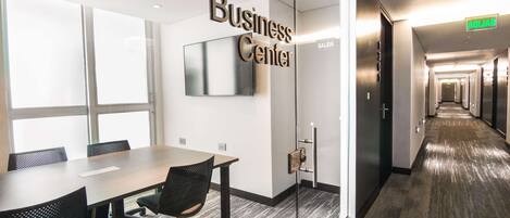 Un centro de negocios con un largo pasillo, una mesa de conferencias con sillas y un letrero que dice "Business Center".