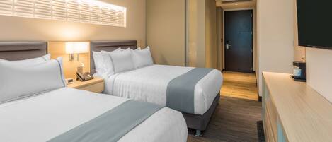 Ett hotellrum med två sängar, ett skrivbord, en lampa, en telefon och en TV.