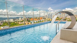 Una piscina en la azotea con vistas a un paisaje urbano, barandillas de metal y una fuente.