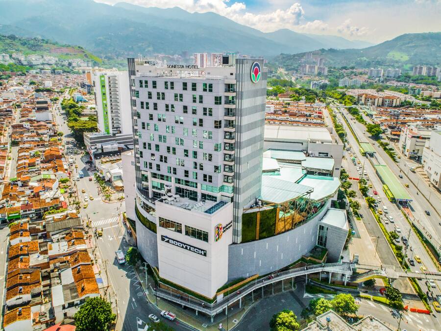 A modern hotel with a rooftop terrace, surrounded by a cityscape and mountains.