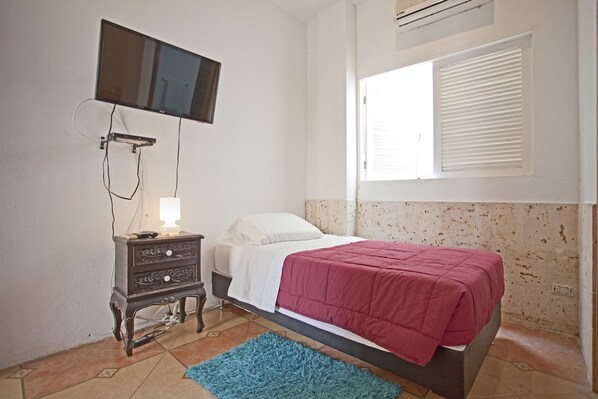 Ein Schlafzimmer mit einem Bett, einem Schminktisch, einem an der Wand befestigten Fernseher und einem Fenster mit Jalousien.