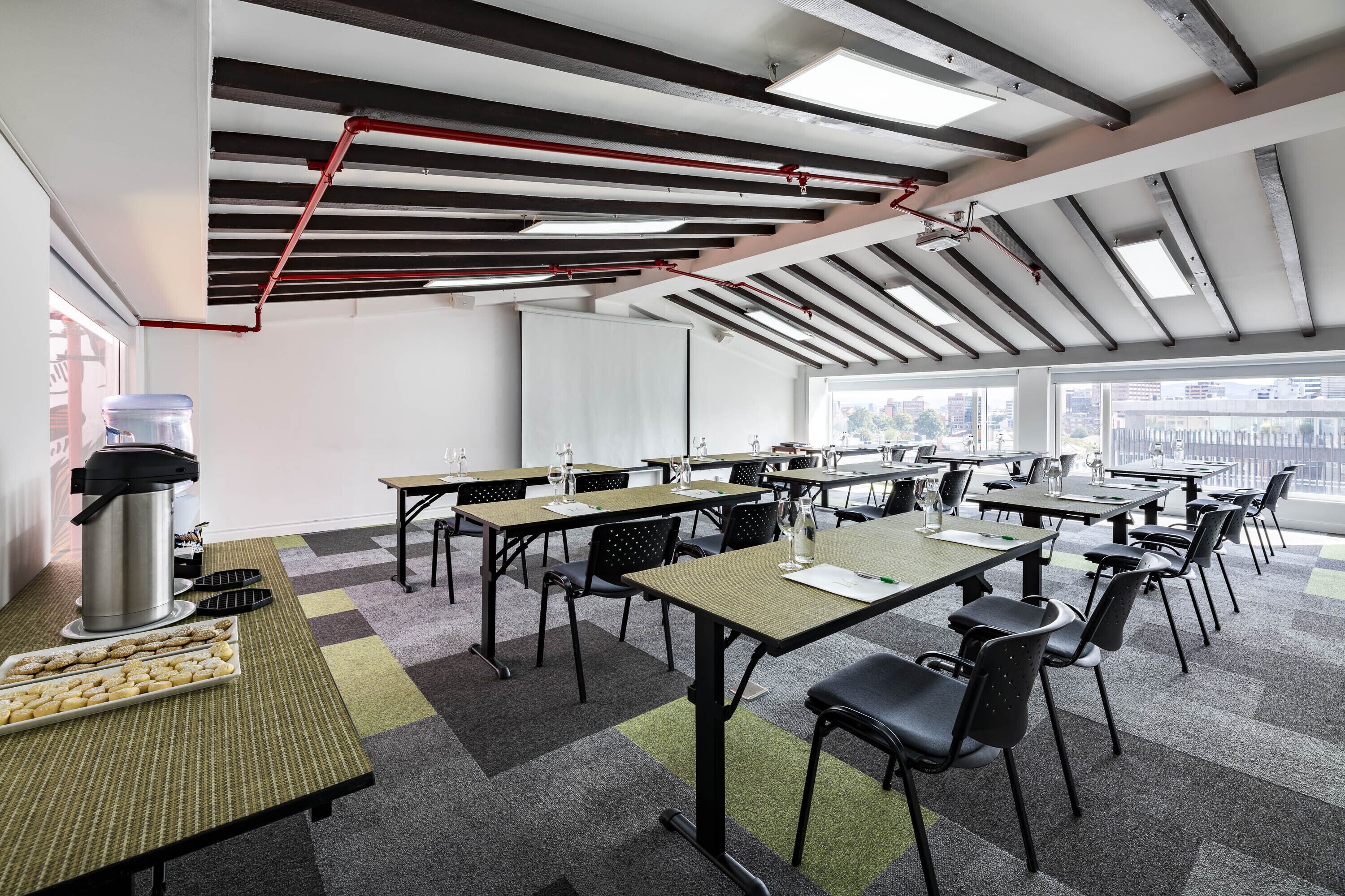 Un salón de conferencias con mesas, sillas, una estación de café y ventanas amplias.