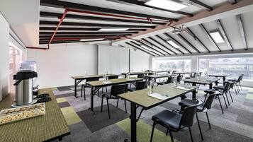 Un salón de conferencias con mesas, sillas, una estación de café y ventanas amplias.