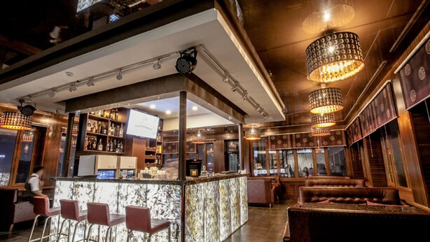 Zona de bar con mostrador de mármol, taburetes y un área de estar con sofá.