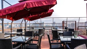 Una terraza al aire libre con mesas y sillas, sombrillas rojas y vistas a la ciudad.